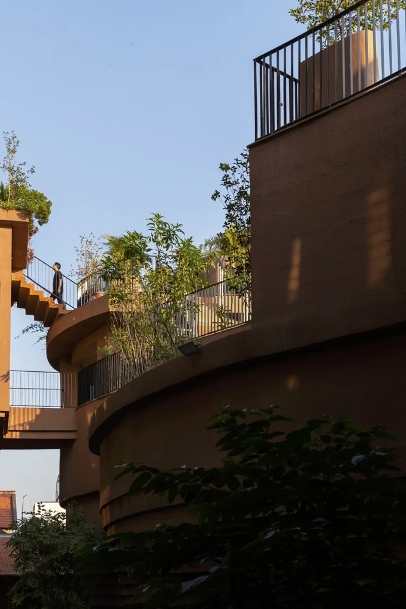 Planted terraces with vertical metal railings ascending the curved facade at dusk