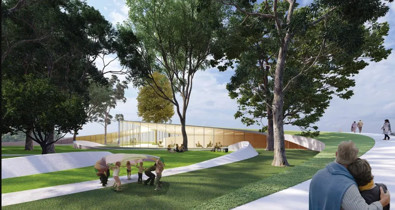 Long low pavilion with translucent golden facade set among existing park trees on a green lawn