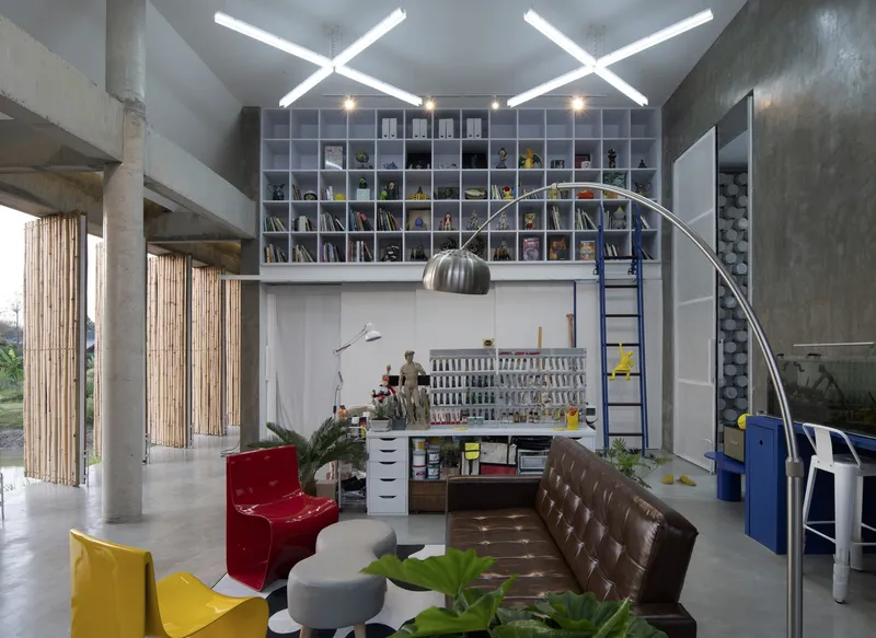 Double-height studio space with concrete columns, vertical bamboo screens and crossed fluorescent light fixtures overhead