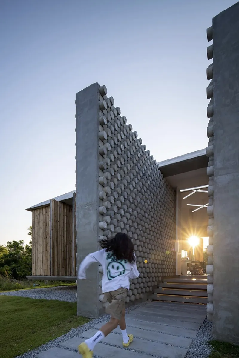 Textured concrete screen wall with hexagonal cutouts at the entry, with a child running by at dusk