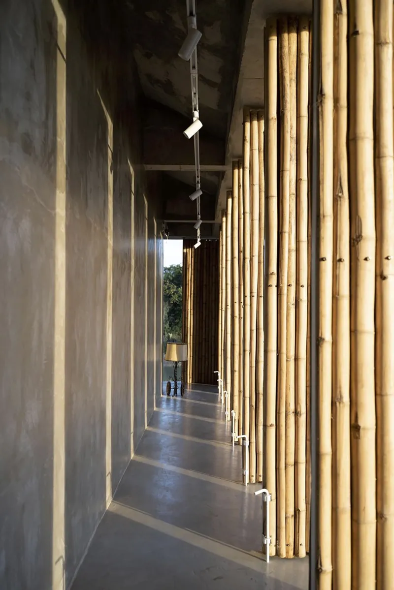 Corridor with concrete walls and vertical bamboo slat screens filtering afternoon light into the passageway