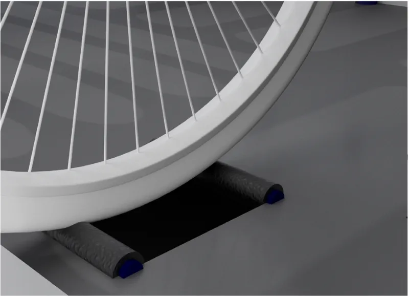 Close-up of a white bicycle wheel resting on two black foam rollers against grey flooring