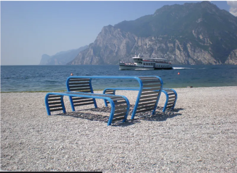 Curved metal benches on a lakeside shore with a passenger boat crossing the water