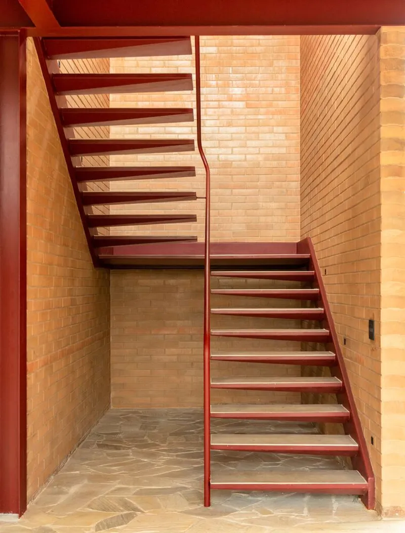 Red steel staircase with timber treads turning through a brick shaft with natural light