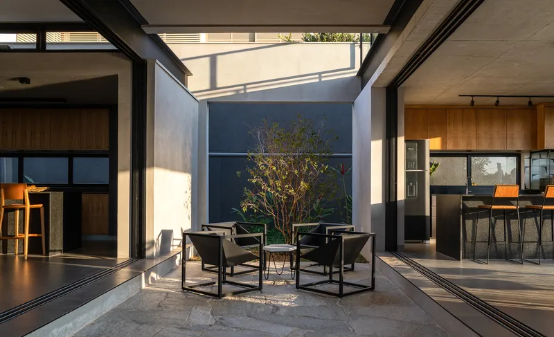 Central courtyard seating area framed by glazed walls, with a small tree and afternoon shadows