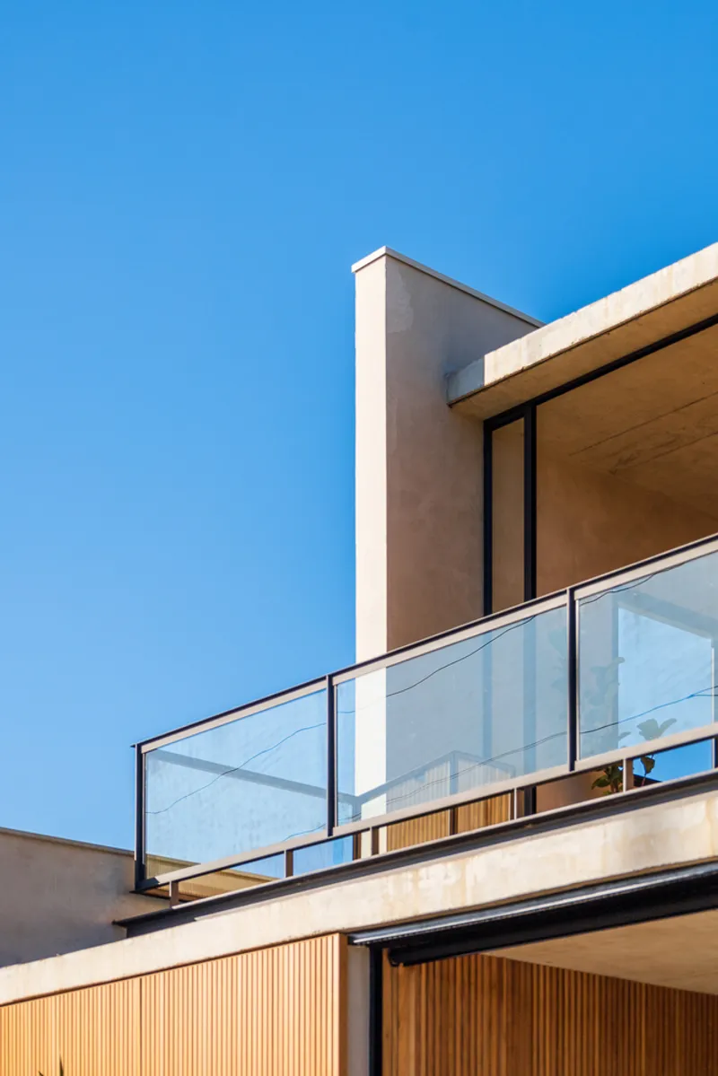 Upper-level balcony with glass balustrade, timber soffit, and vertical chimney element against blue sky