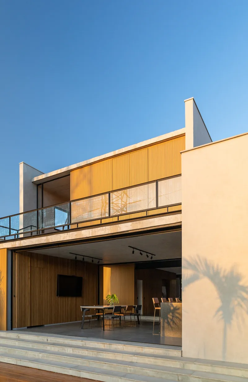 Two-story facade with vertical timber cladding, sliding glass doors, and upper terrace under late afternoon sun