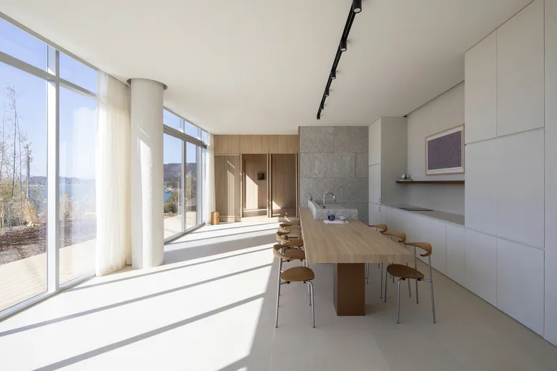 Dining area with timber table and white cabinetry flooded with morning sunlight through floor-to-ceiling glazing