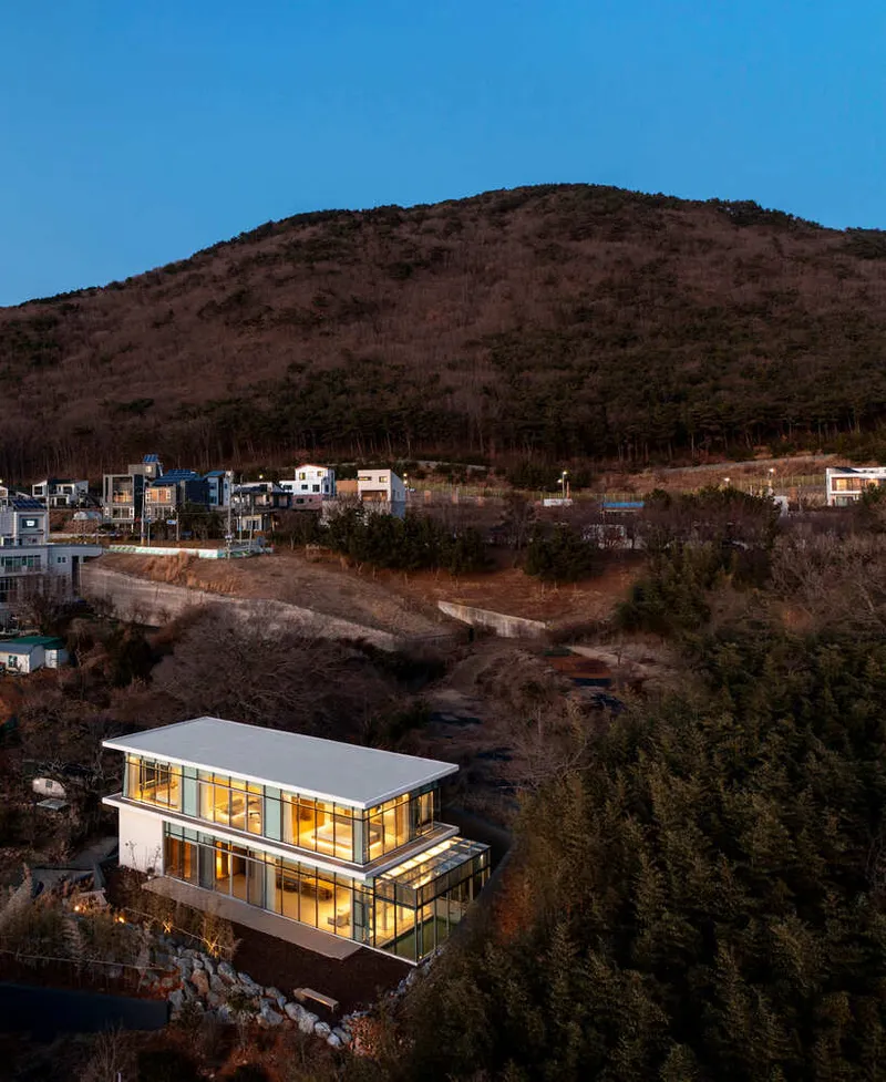 Elevated view of the illuminated two-story residence on a wooded hillside at dusk