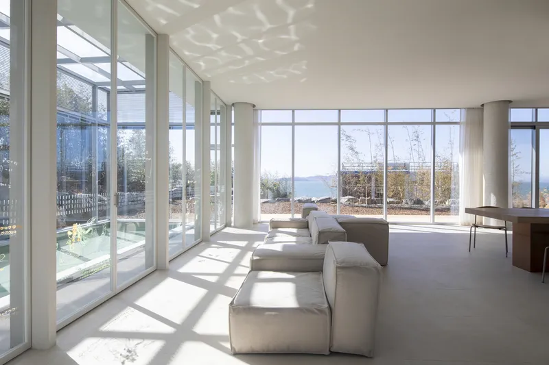 Living room with modular seating and dappled sunlight filtering through latticed screens overlooking water