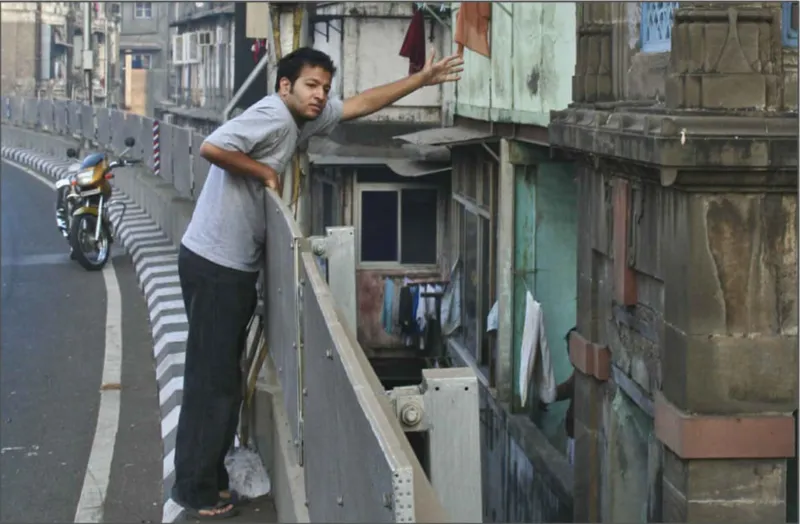 Man reaching toward a patchwork facade of weathered panels and windows beside a highway guardrail