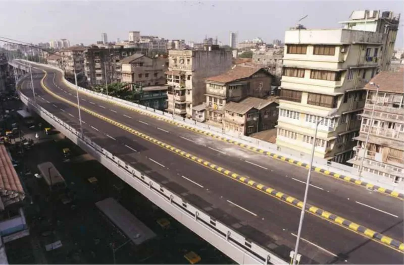 Elevated highway deck threading through dense urban housing blocks under pale morning light