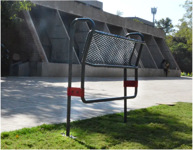 Tubular steel exercise equipment with mesh platform and red brackets on a lawn near a concrete facade