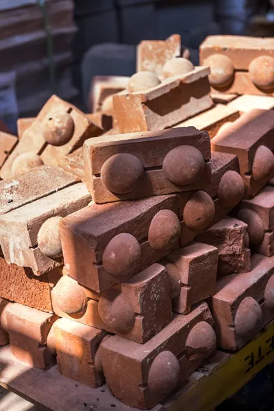 The image showcases a stack of red bricks, each featuring two prominent circular elements. The brick