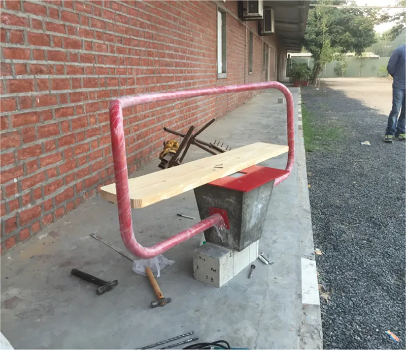 Prototype bench under construction with pink-wrapped steel frame and timber plank beside a brick wall