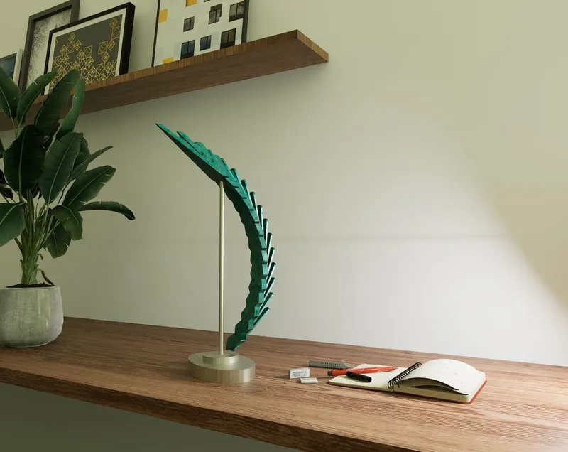 Teal wing sculpture on a wooden desk beside an open notebook and potted plant