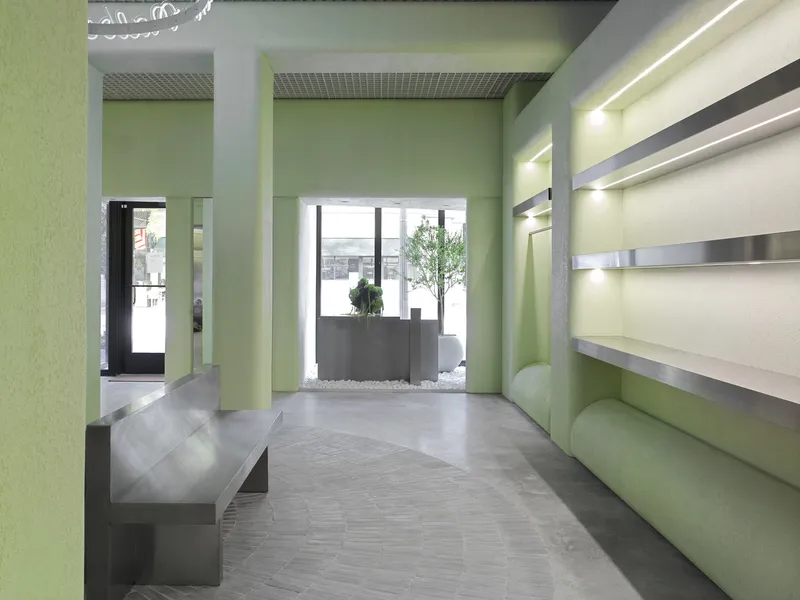 View through pale green columns toward street entrance with planted reception desk and natural daylight
