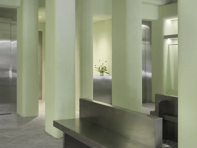 Gray metal bench between pale green columns with planted display niche in background