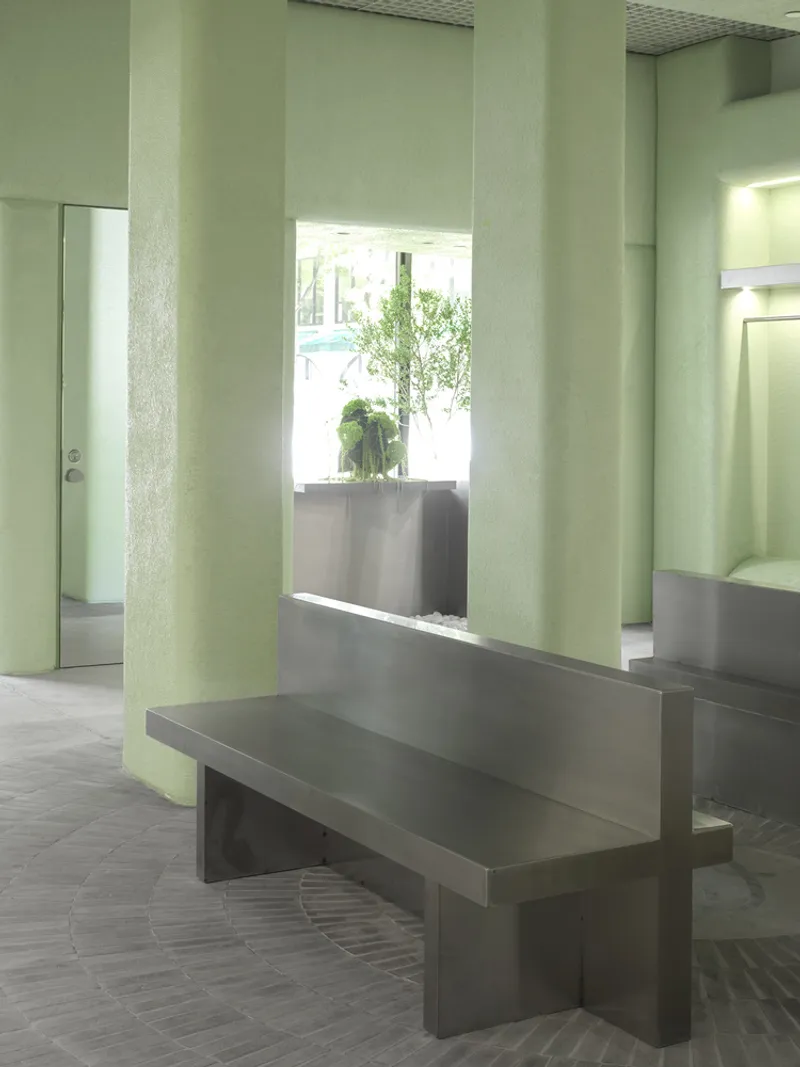 Metal bench beside pale green column with view to planted window niche and mirrored wall