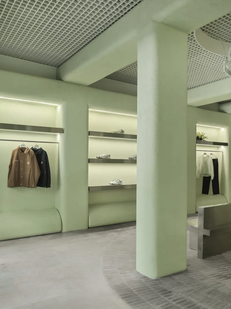 Retail space with metal grid ceiling, backlit display niches, and pale green upholstered seating
