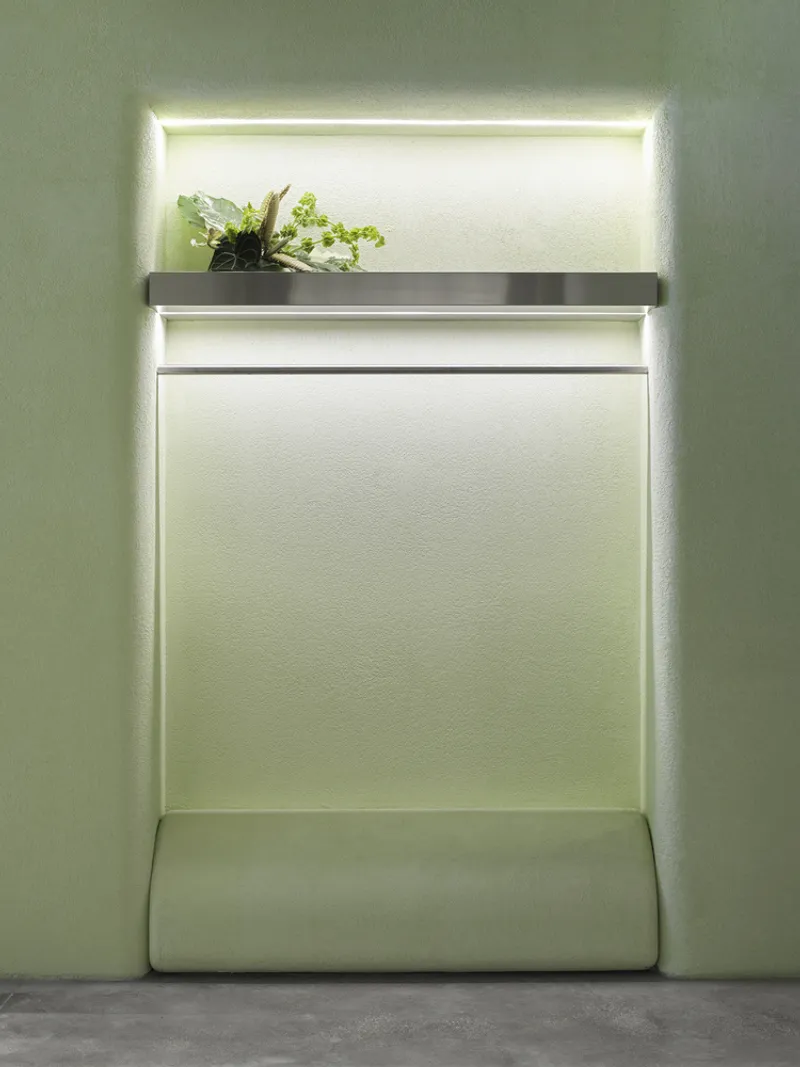 Backlit wall niche with metal shelf holding potted fern above upholstered bench seat