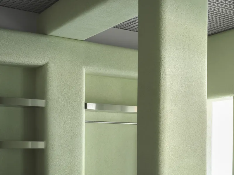 Pale green textured plaster walls with horizontal metal bands and perforated ceiling panels with sunlight