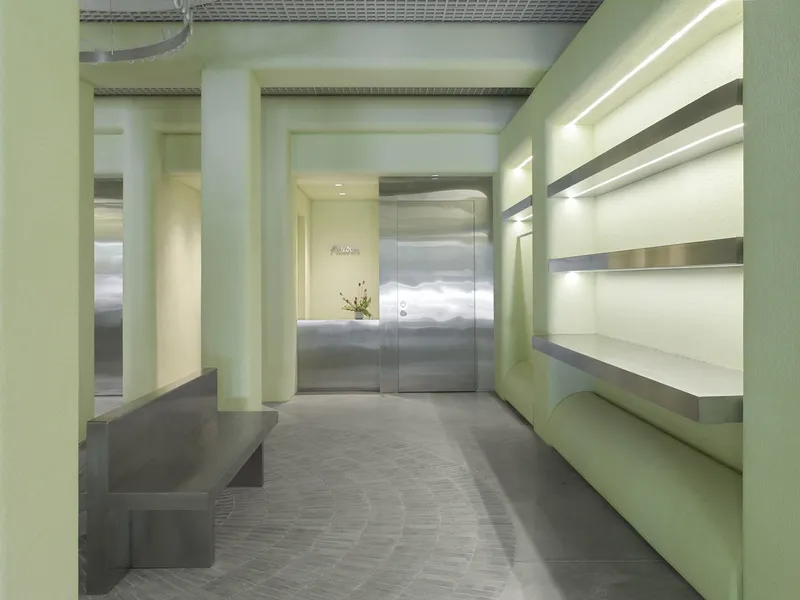 Entry lobby with pale green walls, polished metal elevator doors, built-in seating, and herringbone stone flooring