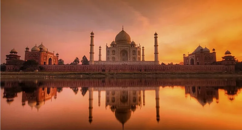 Riverfront view of domed mausoleum complex with minarets reflected in water at sunset