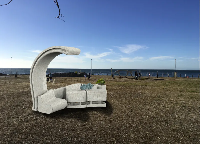 Sculptural concrete bench with curved canopy on a grassy waterfront with ocean and blue sky beyond