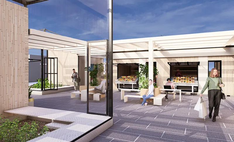 View through open steel-framed glass door into the courtyard with market stalls and timber-clad volumes