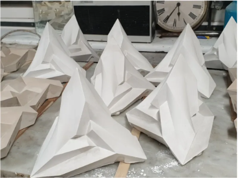 Close-up of white faceted plaster sculptures arranged on a work surface with visible dust