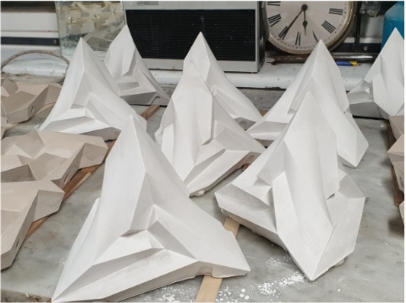 Close-up of white faceted plaster sculptures arranged on a work surface with visible dust