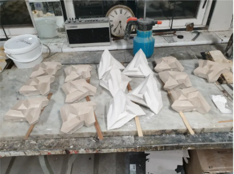 Workbench view showing multiple plaster prototypes in white and tan beside power tools and computer
