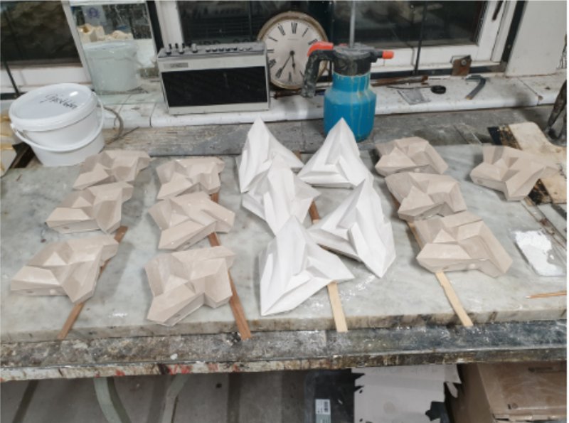 Workbench view showing multiple plaster prototypes in white and tan beside power tools and computer