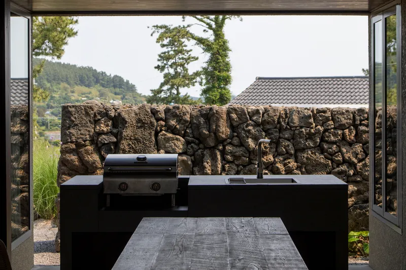 View through open doors to outdoor kitchen counter backed by volcanic stone wall with hillside beyond