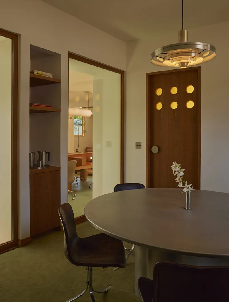 Round table with pendant light fixture and walnut door punctuated by six circular brass portholes