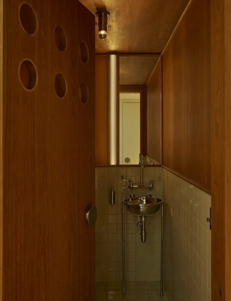 Compact bathroom with wall-mounted brass basin and walnut paneling with circular cutouts