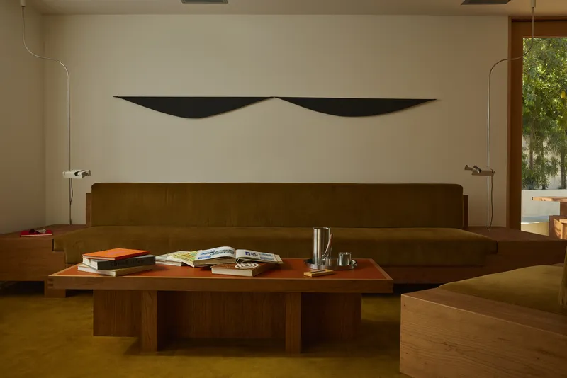Walnut banquette and low table on olive carpet with black sculptural wall relief above
