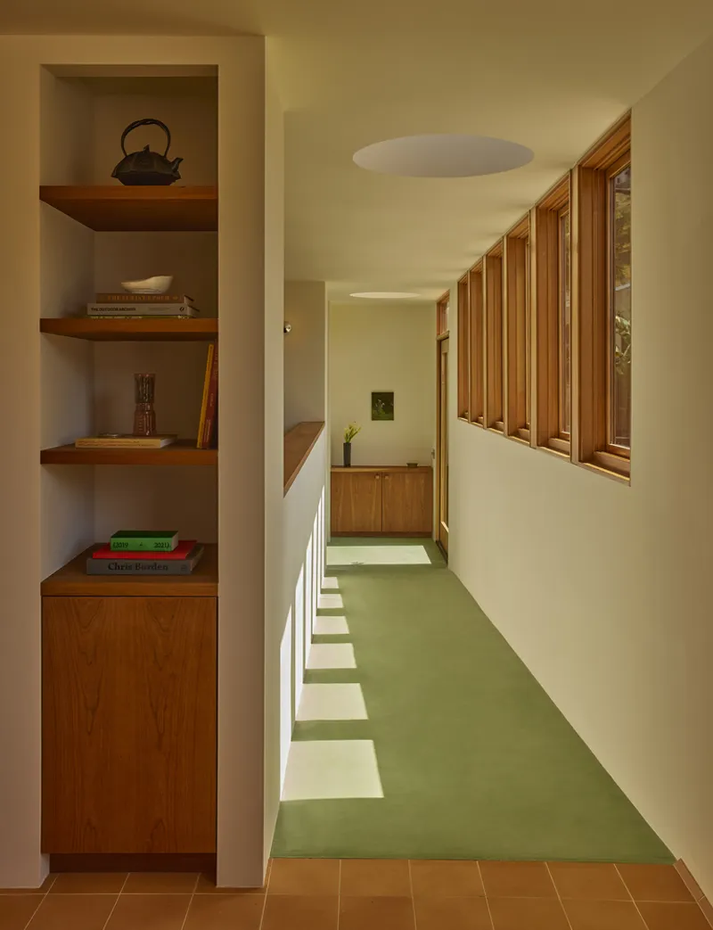 Corridor with built-in timber shelving and vertical timber slat windows overlooking greenery