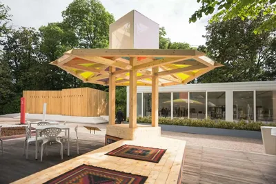 This architectural image showcases a contemporary pavilion with a wooden structure and a colorful ca