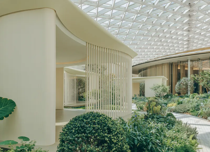 Interior courtyard with curved vertical screens and planted beds under a geometric glass skylight