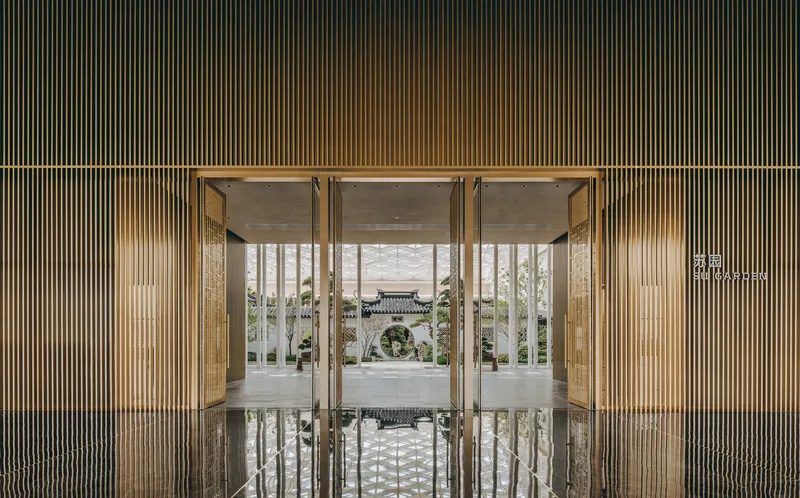 Glass vestibule framed by vertical timber louvers reflecting on polished stone floor