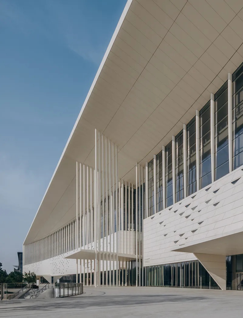 Cantilevered facade with vertical white fins and perforated panel cladding beneath a clear blue sky