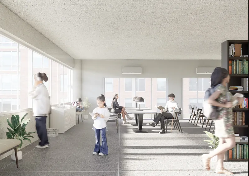 Shared community room with long table and bookshelves filled with daylight from tall windows