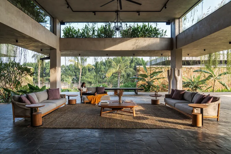 Open-air lounge with concrete canopy and planted clerestory band filtering afternoon sunlight