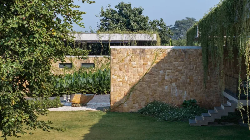 Stone boundary wall with stepped access beside lawn and trailing vines under afternoon sky