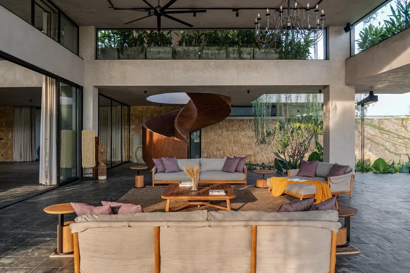Double-height living area with helical copper stair beneath concrete bridge linking upper level planted terraces