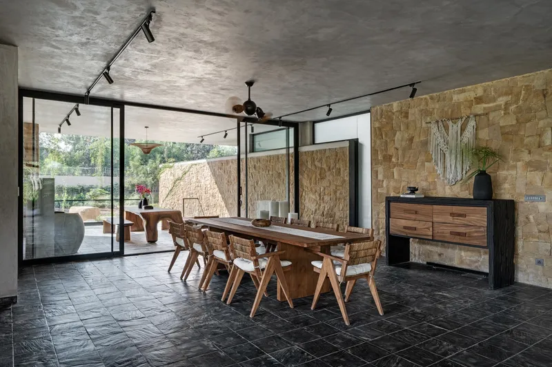 Dining room with sandstone block wall and black tile floor opening to courtyard through steel-framed doors