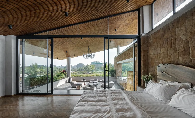 Bedroom with slatted timber ceiling and stone wall overlooking covered terrace and green hillside