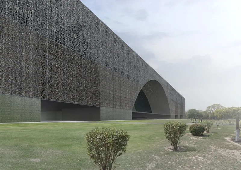 Long view of the perforated stone facade with deep arched entry and scattered shrubs in the landscape
